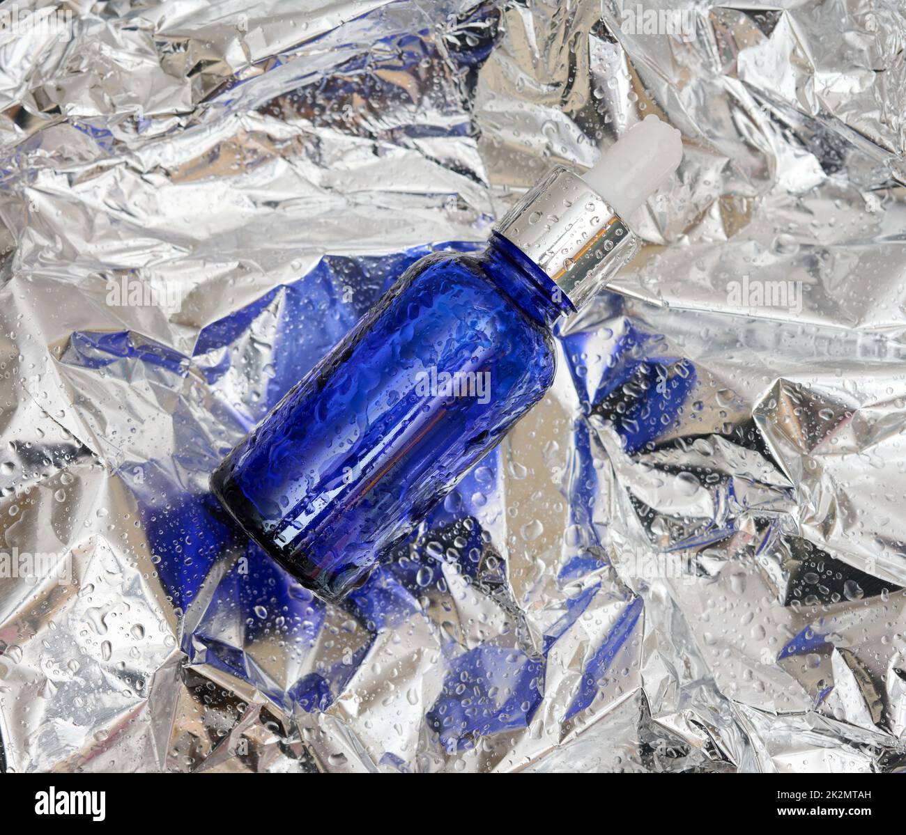 Blaue Glasflasche Pipette vor dem Hintergrund der zerknitterte graue Folie . Apothekenkonzept. Kollagenhaut. Mockup Hautpflege kosmetisches Produkt Stockfoto