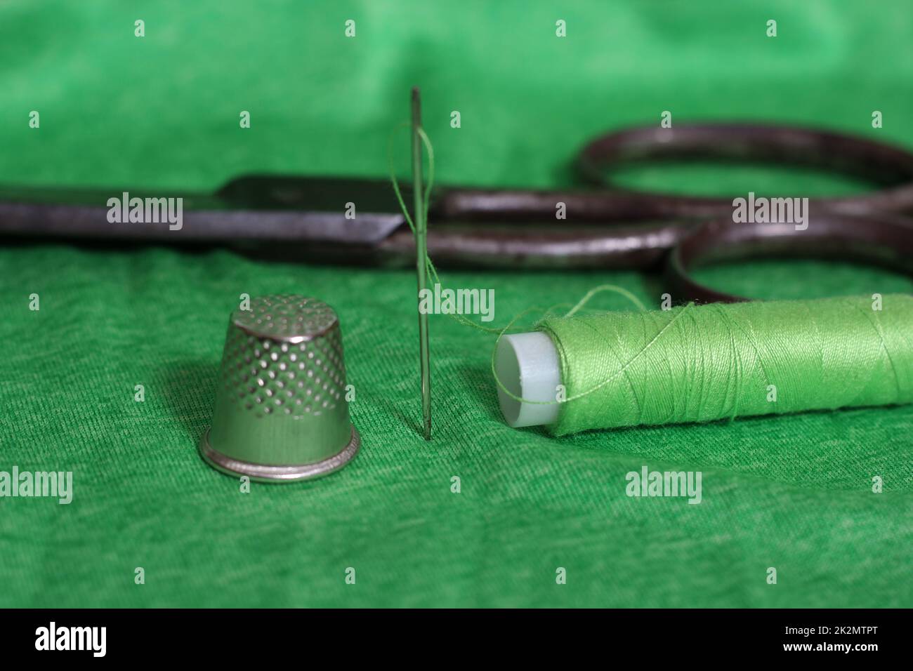 Spule aus grünem Faden, Nimble und Nadel auf grünem Stoff Stockfoto