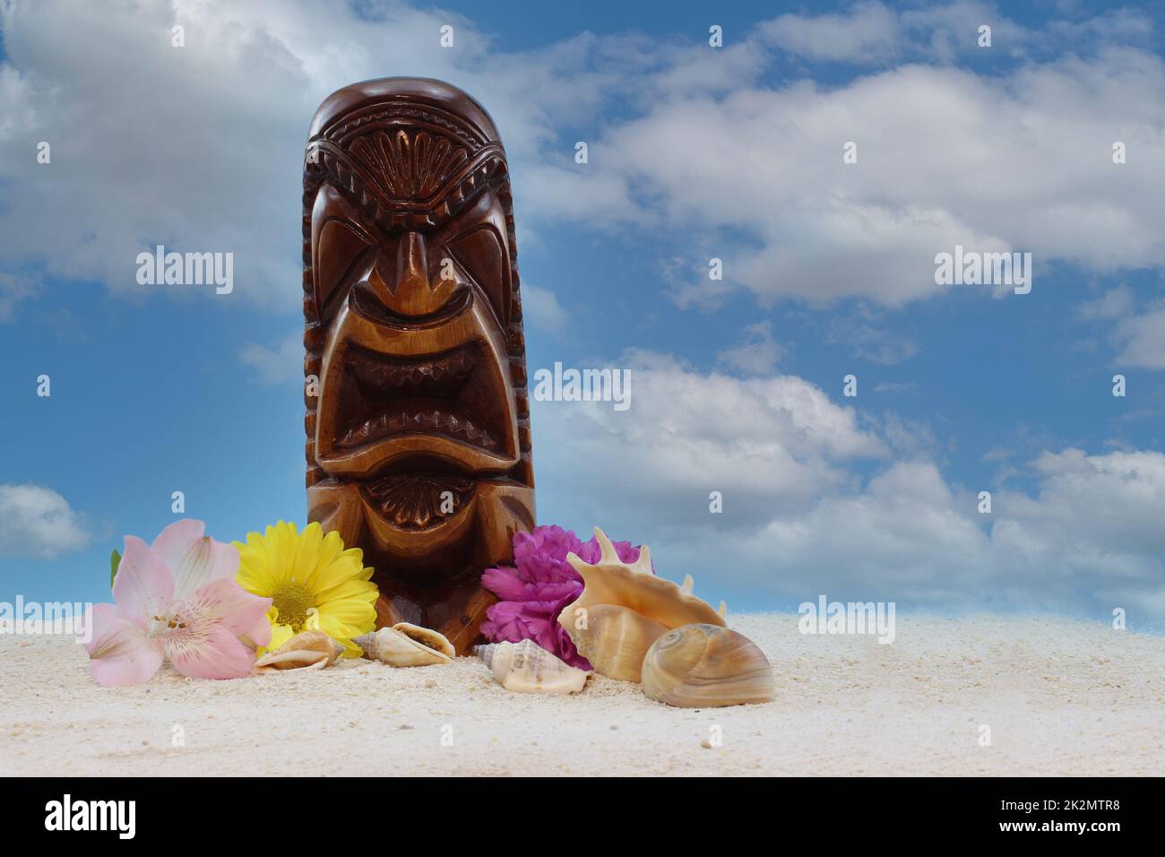 Antike Holzmaske aus Hawaii am Strand mit Blumen und blauem Himmel Stockfoto