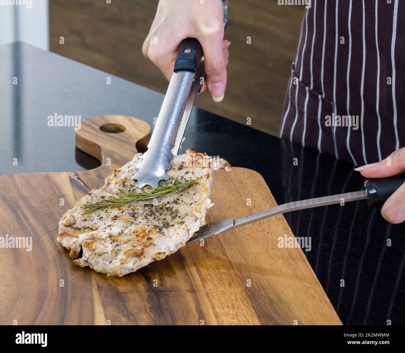 Das gekochte Schweinesteak wird auf ein hölzernes Schneidebrett gestellt. Nahaufnahme Stockfoto