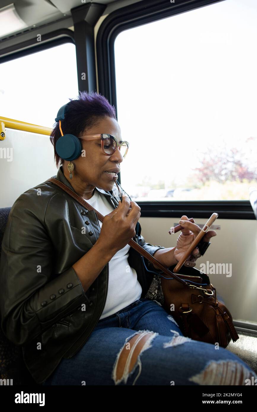 Beifahrerin, die Lippenglanz mit Smartphone auf öffentlichen Bus anwendet Stockfoto