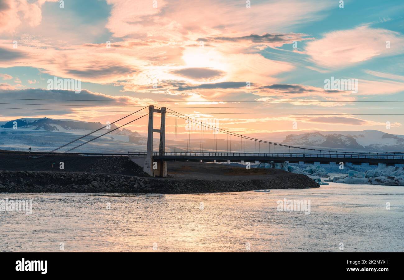 Wunderschöner Sonnenuntergang über der Hängebrücke auf der Gletscherlagune des Jokulsarlon mit Eisberg, der im Süden des Vatnajokull National Park auf Island schwimmt Stockfoto