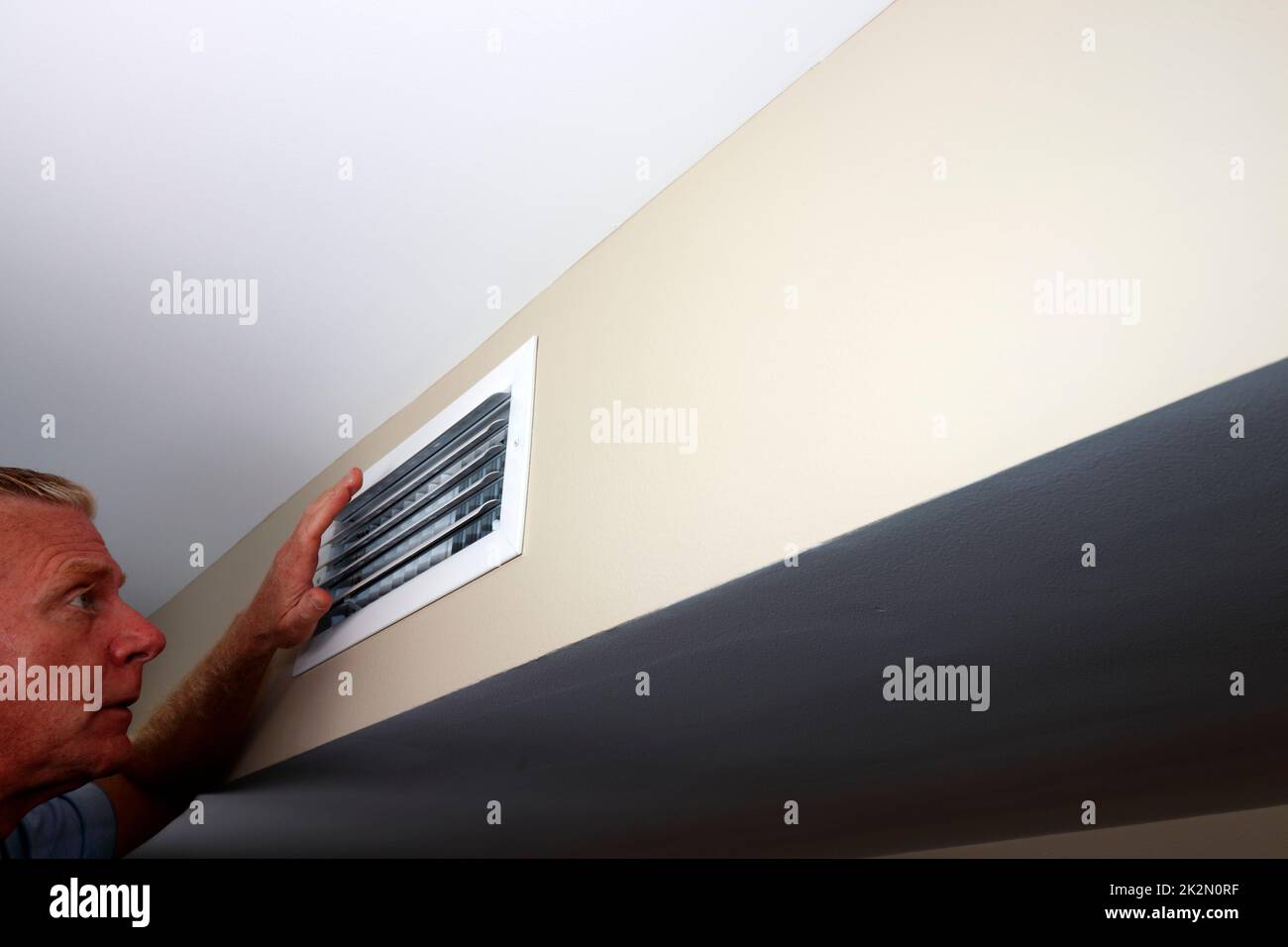 Ein Mann, der in einen Wall-Home-Lüftungsschacht schaut, während er eine Hand hochhält Stockfoto