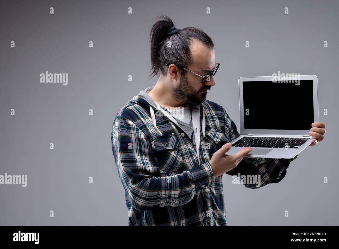 Ein Mann mit Pferdeschwanz und Brille, der einen Laptop in der Hand hat Stockfoto
