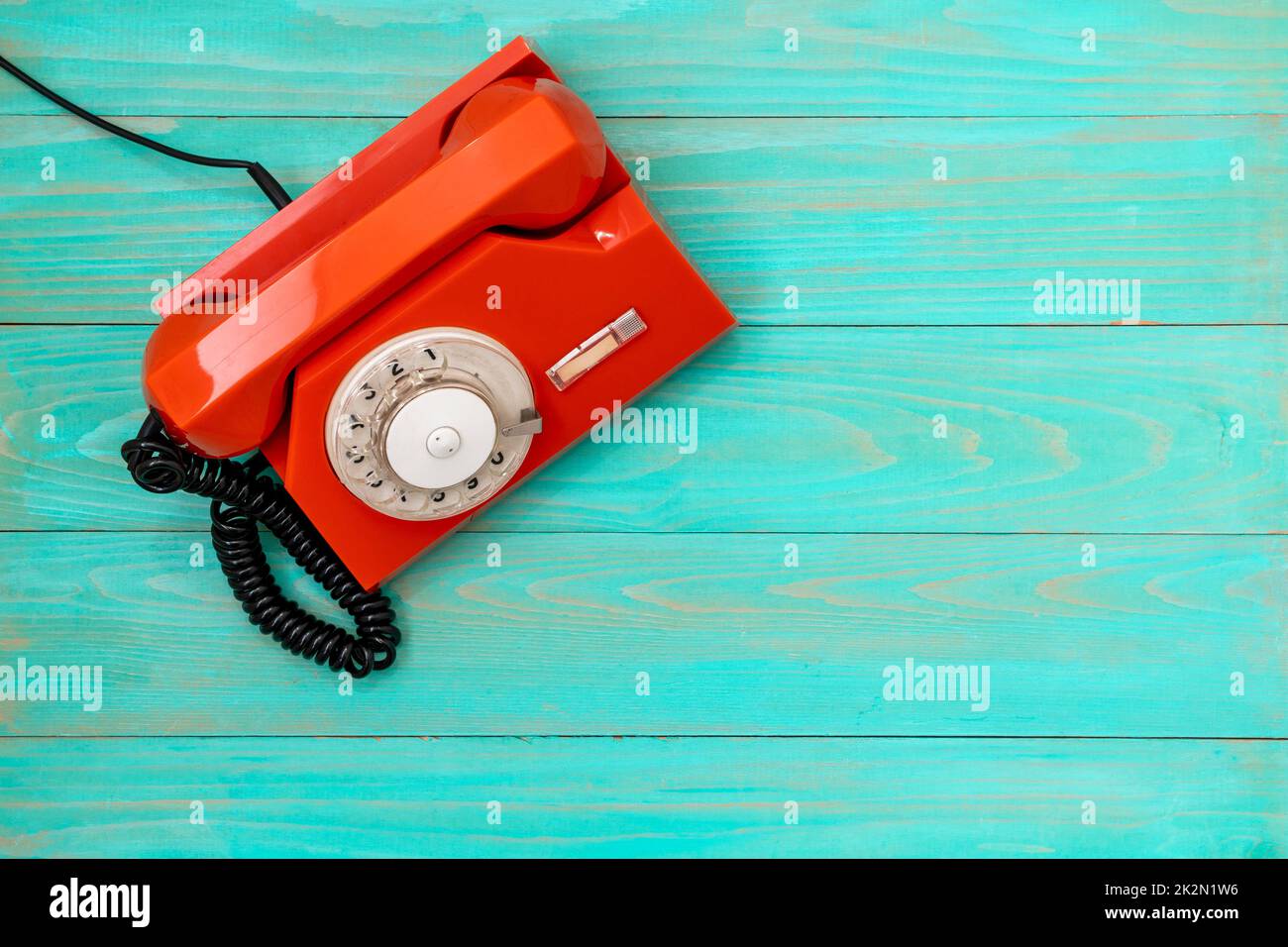 Altes, orangefarbenes Drehwahltelefon auf blauem Holzhintergrund Stockfoto