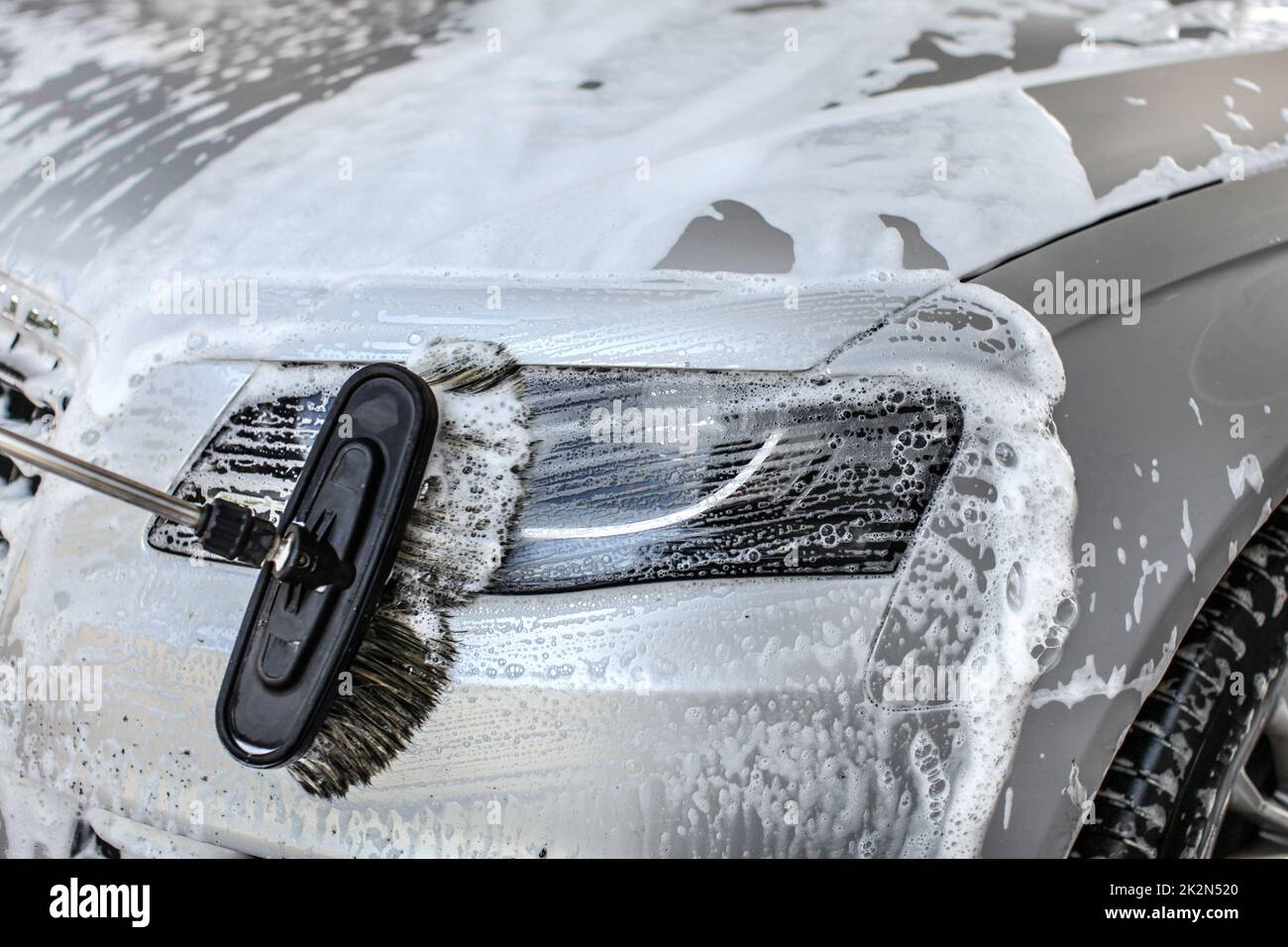 Auto gereinigt bei manuellen Autowäsche Bürste aus Anschläge in Shampoo auf der vorderen Beleuchtung Glas. Stockfoto