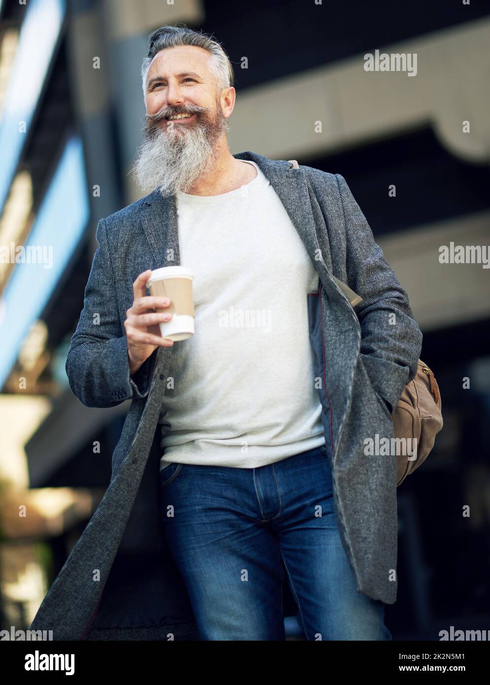 Selbstbewusster, reifer Geschäftsmann, der in der Straße in der Stadt mit Kaffee unterwegs ist und den urbanen Lebensstil genießt Stockfoto