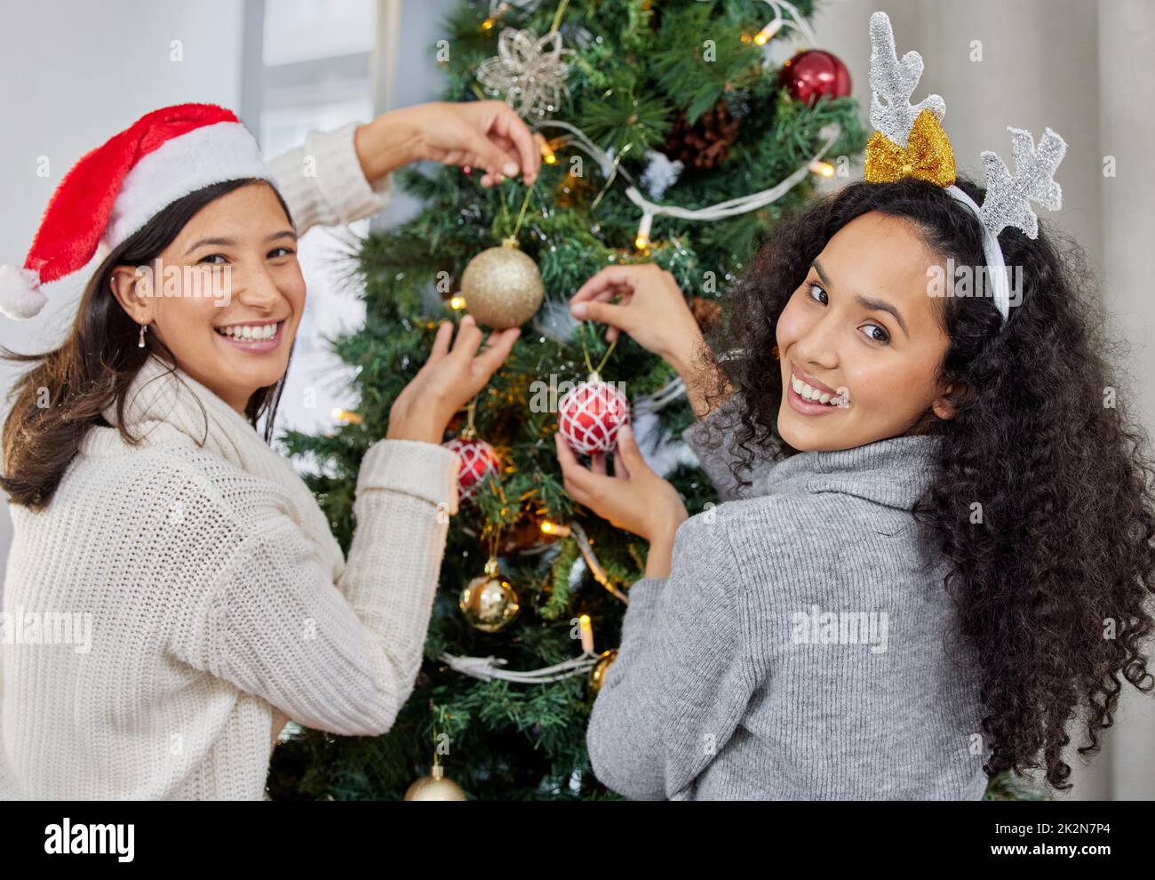 Zeit, den Baum zu schmücken. Aufnahme von zwei jungen Frauen, die den Weihnachtsbaum zu Hause schmücken. Stockfoto