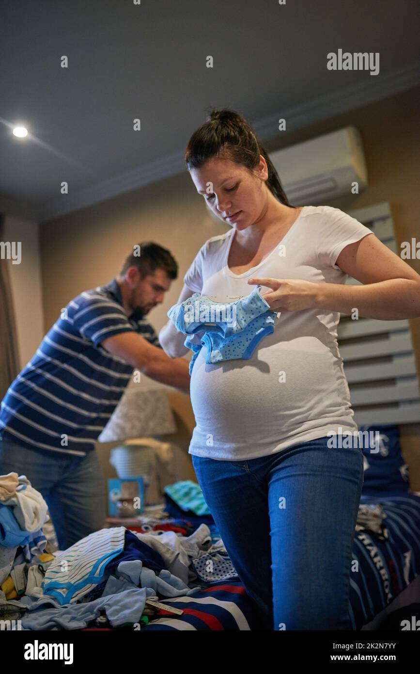 Sortierte den Kleiderschrank für Babys. Aufnahme eines liebenden, Schwangeren Paares, das zu Hause Babykleidung zusammenfaltet. Stockfoto