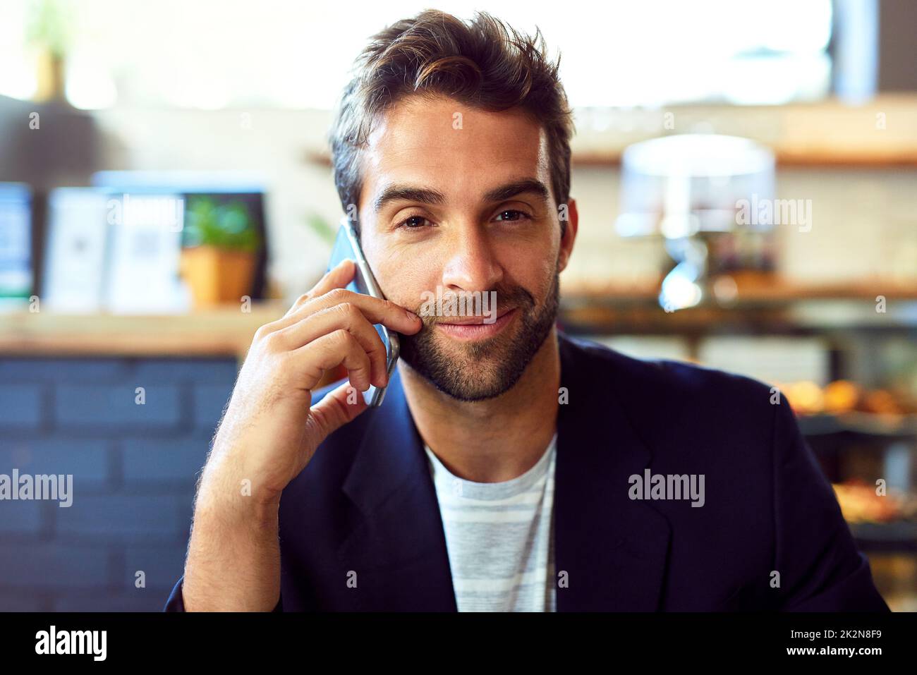 Treffen Sie mich zum Kaffee. Porträt eines hübschen jungen Mannes, der in einem Café telefoniert. Stockfoto