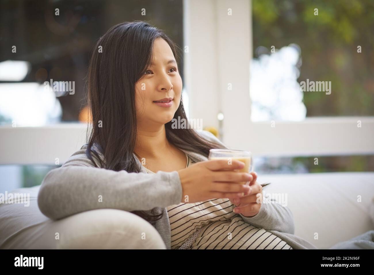 Genießen Sie einen ruhigen und gemütlichen Moment zu Hause. Aufnahme einer Schwangeren, die nachdenklich aussieht, während sie zu Hause ein warmes Getränk trinkt. Stockfoto