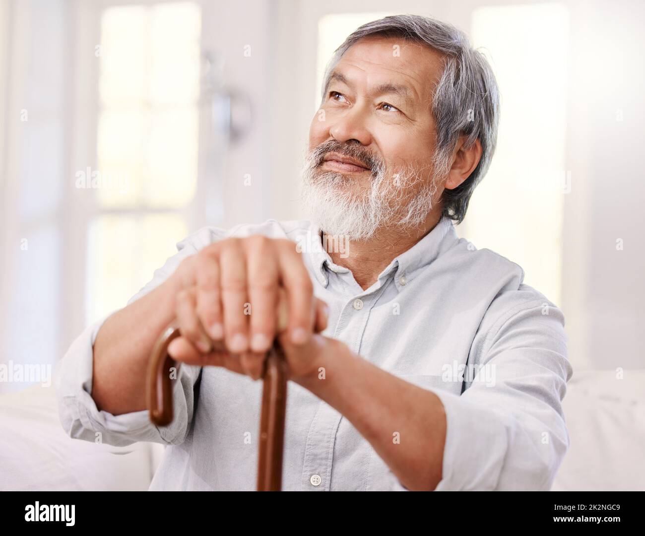 Ich freue mich auf den heutigen Tag. Aufnahme eines älteren Mannes, der zu Hause mit einem hölzernen Spazierstock sitzt. Stockfoto