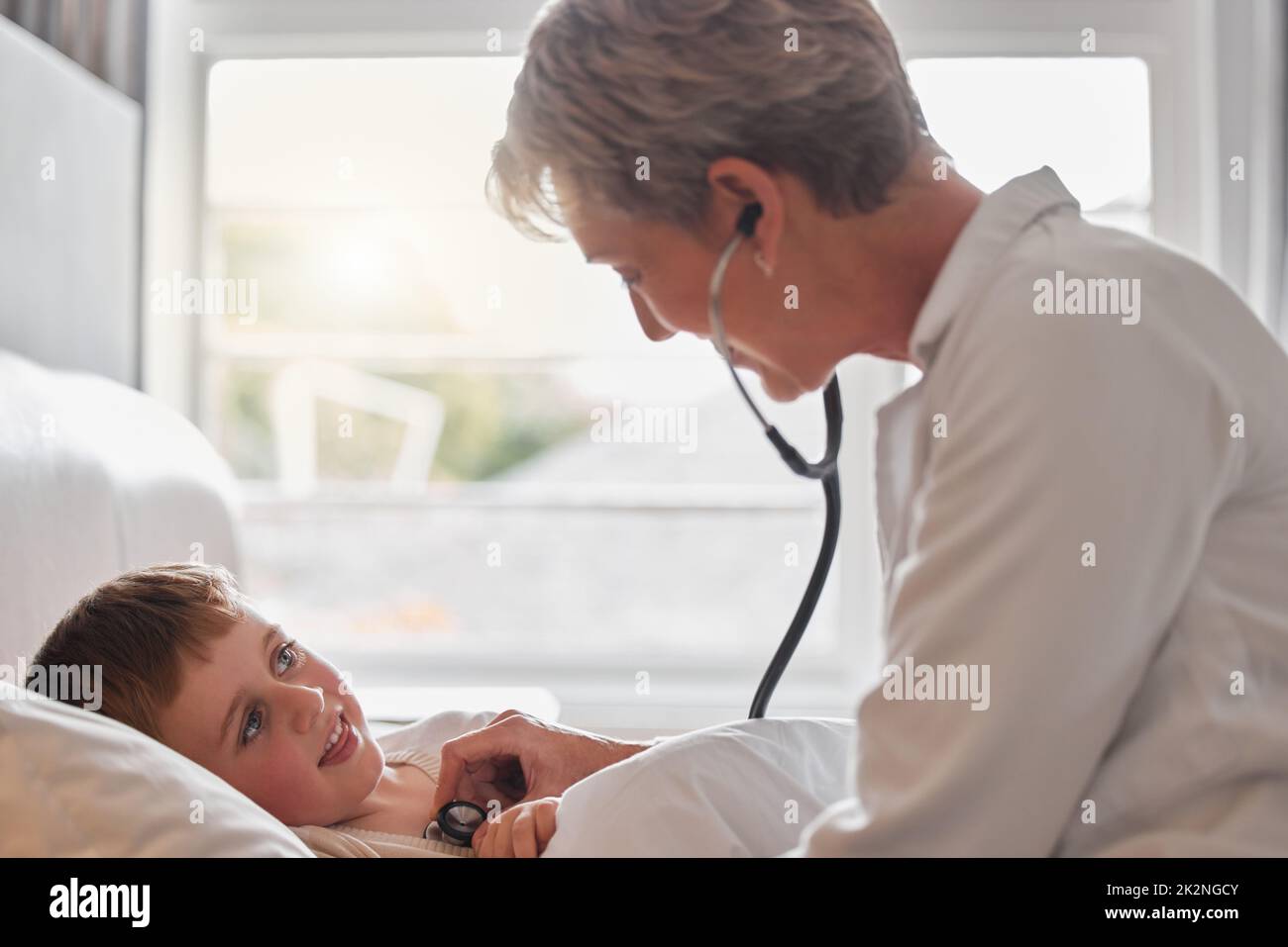 Dieses große Junge fühlt sich heute. Aufnahme eines Arztes Untersuchung eines kleinen Jungen mit einem Stethoskop im Bett zu Hause. Stockfoto