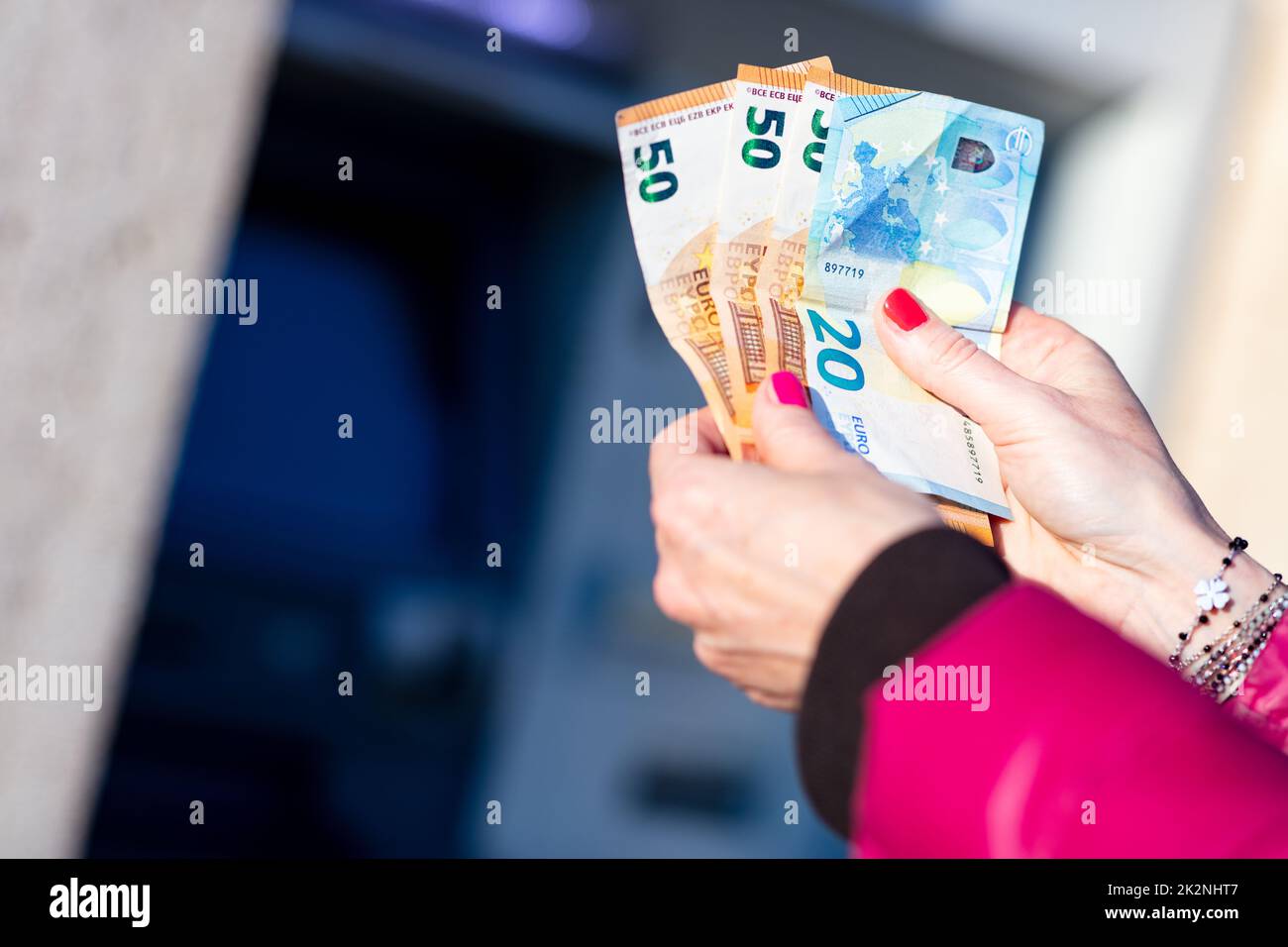 Banknoten in den Händen einer Frau neben einem Geldautomaten Stockfoto