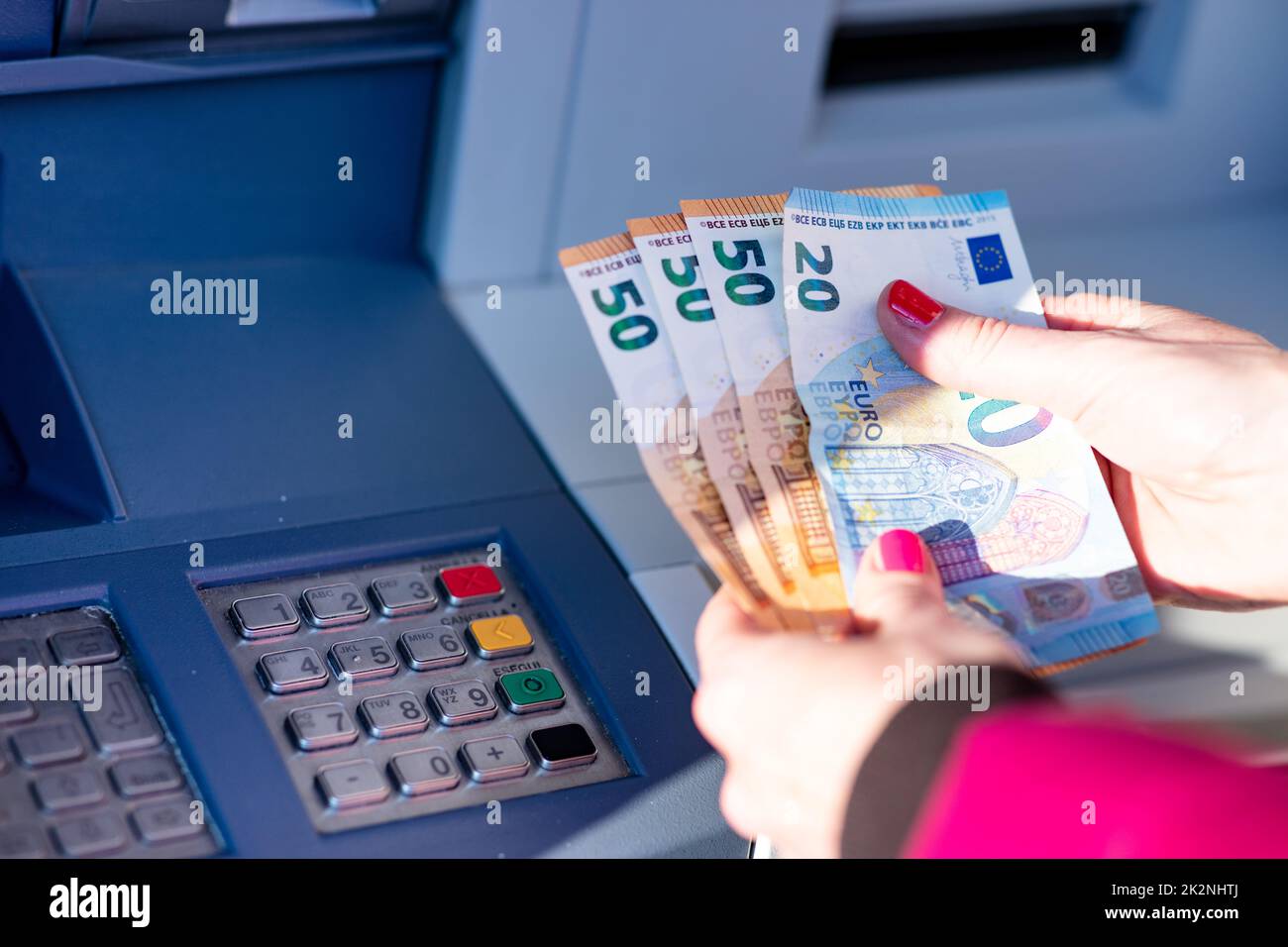 Banknoten in den Händen einer Frau neben einem Geldautomaten Stockfoto