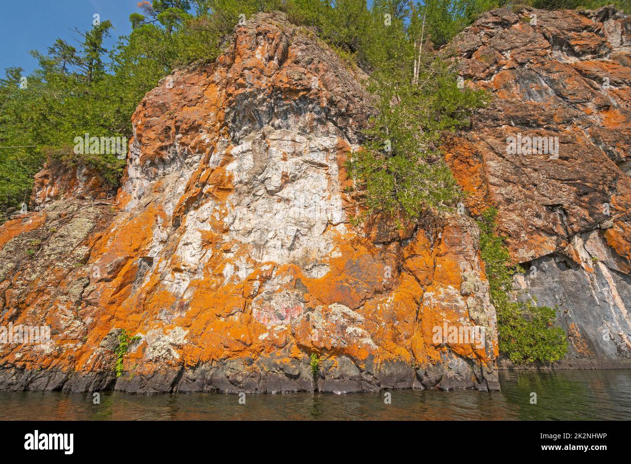 Lichen Colored Cliffs an einem abgelegenen Seeufer Stockfoto