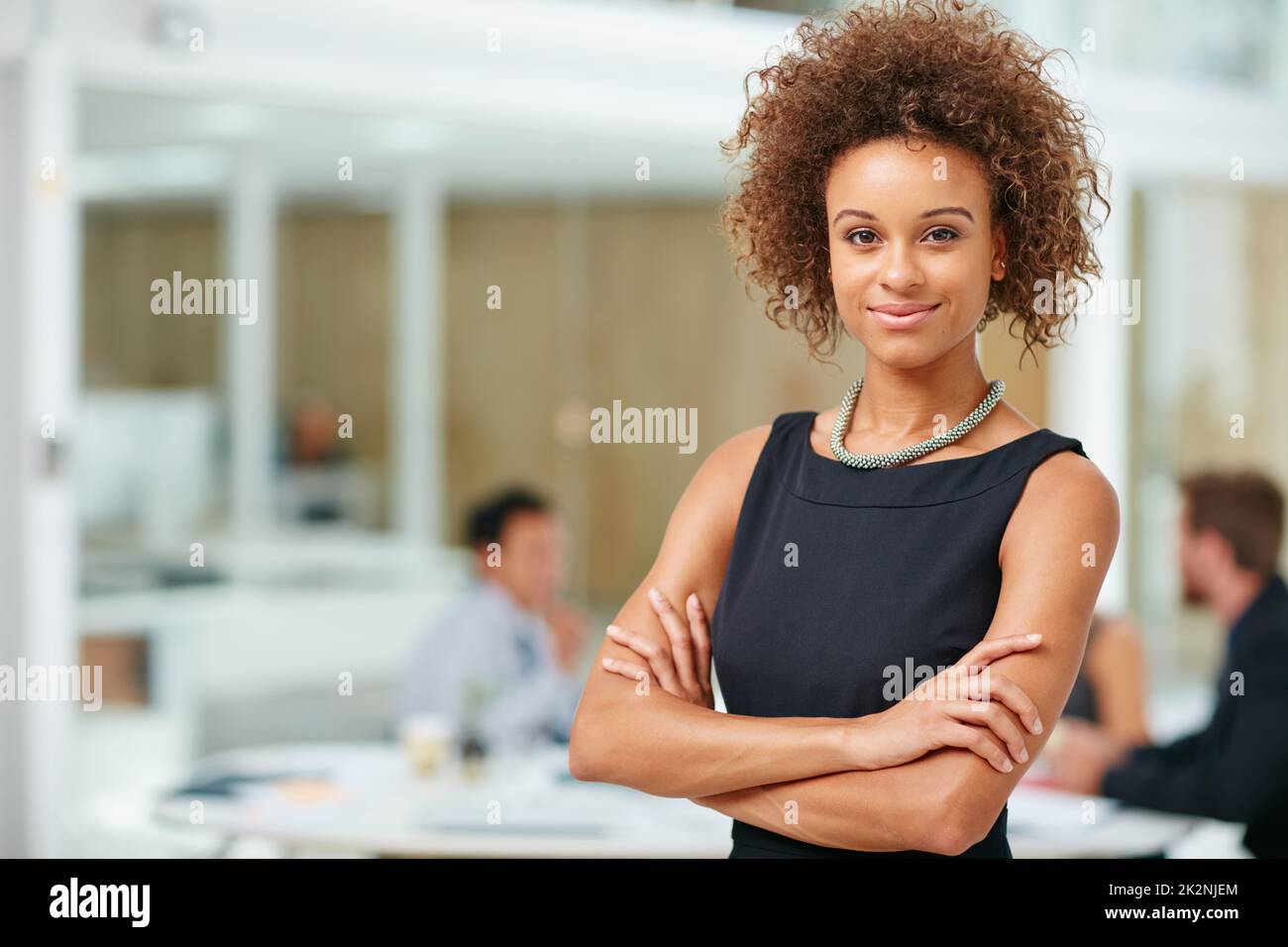 Sie baut ihre Karriere an einem Arbeitstag nach dem anderen auf. Porträt einer lächelnden jungen Geschäftsfrau, die mit gekreuzten Armen in einem modernen Büro steht. Stockfoto