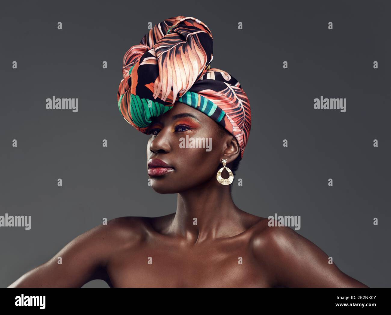 Ja, du kannst feminin sein und immer noch wild sein. Studiofoto einer wunderschönen jungen Frau, die eine traditionelle afrikanische Kopfummantelung vor grauem Hintergrund trägt. Stockfoto
