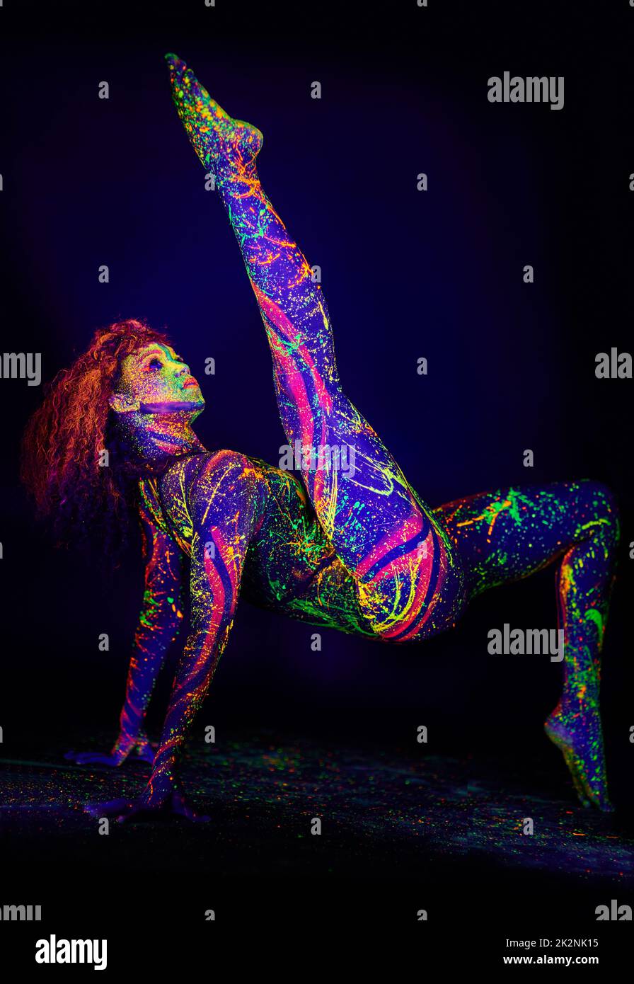 Schätze im Dunkeln. Ganzkörperaufnahme einer jungen Frau, die mit Neonfarbe auf ihrem Gesicht posiert. Stockfoto