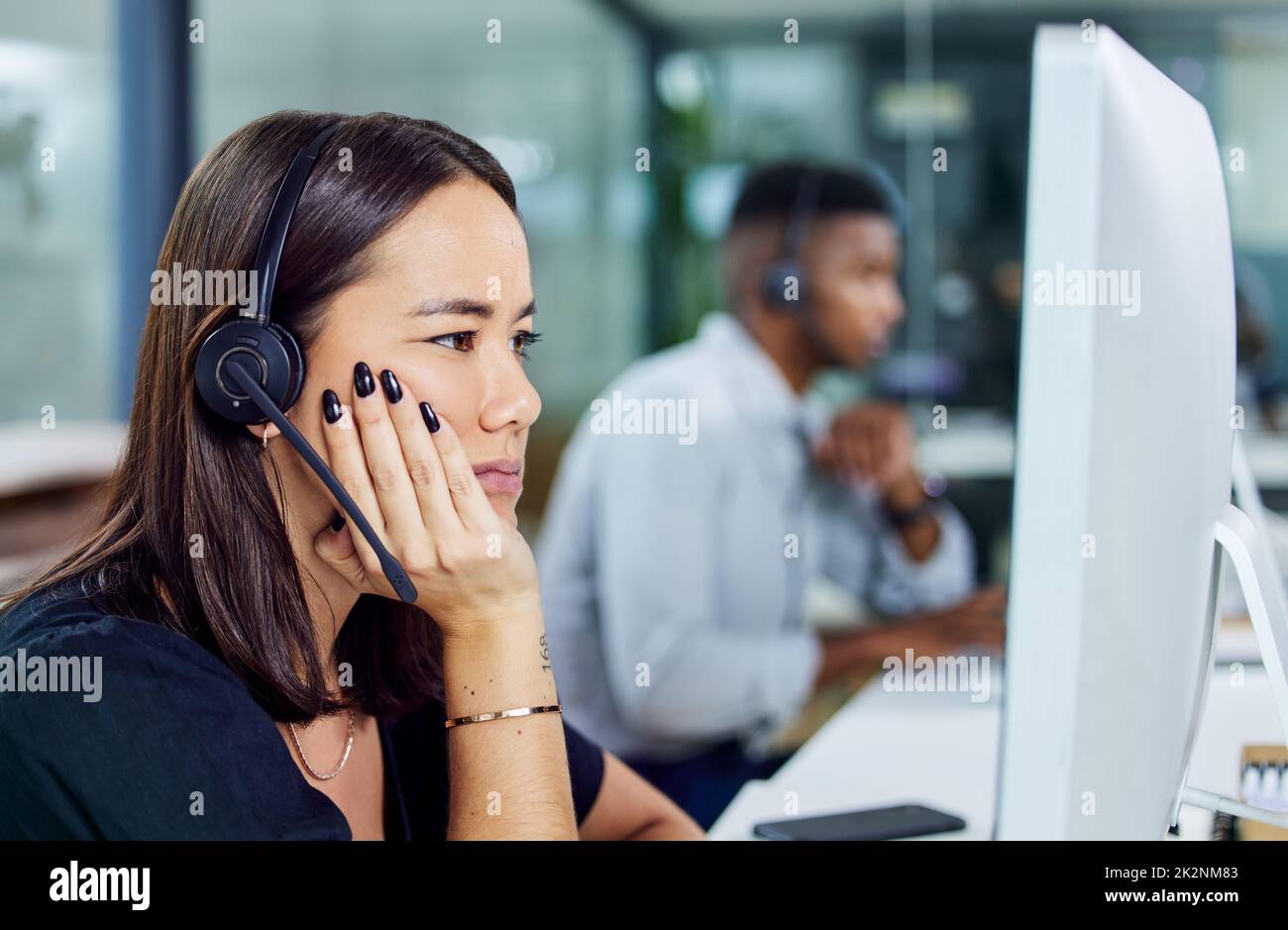 Wann ist dieser Tag zu Ende. Aufnahme eines jungen Callcenter-Agenten, der verwirrt aussieht, während er einen Desktop-pc im Büro verwendet. Stockfoto