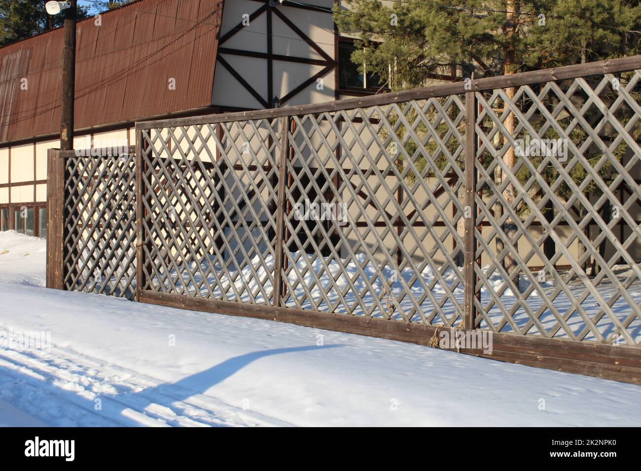 Wunderschönes helles Haus mit einem rötlich-braunen Dach und einem gemusterten geschnitzten Zaun. Im Winter. Stockfoto