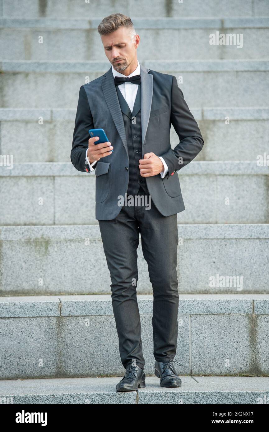 Eleganter Mann in Fliege Anzug im Freien. Geschäftsmann Mann mit Telefon. Mann Chef im Chat auf dem Smartphone Stockfoto