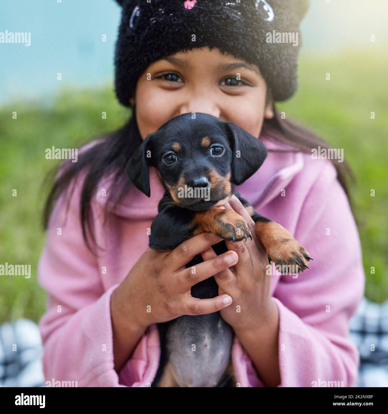 Glück ist ein zappelnder Welpe. Das verkürzte Porträt eines niedlichen kleinen Mädchens, das ihren Welpen kuschelt, während es draußen sitzt. Stockfoto