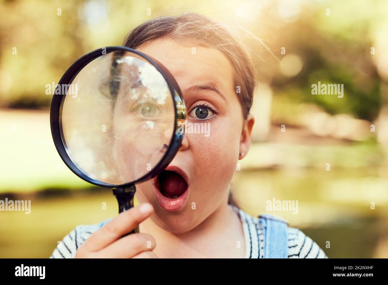 Neugierig auf die Welt. Porträt eines kleinen Mädchens, das erstaunt durch eine Lupe schaut. Stockfoto