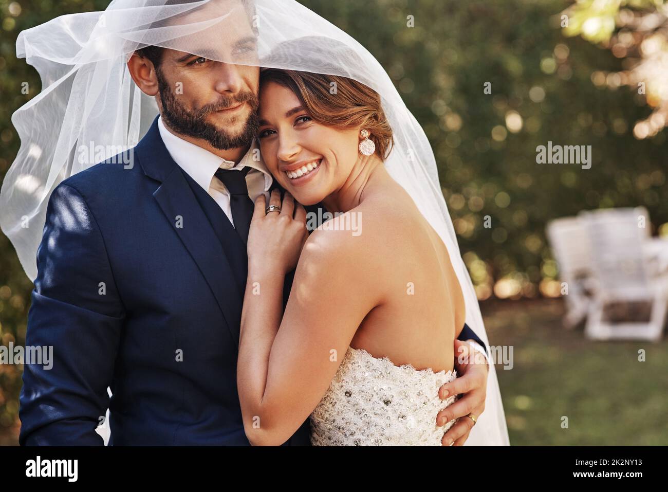 Ich bin so froh, dass ich ihn geheiratet habe. Ausgeschnittene Aufnahme einer anhänglichen jungen Braut, die am Hochzeitstag lächelt und ihren Bräutigam unter einem Schleier umarmt. Stockfoto