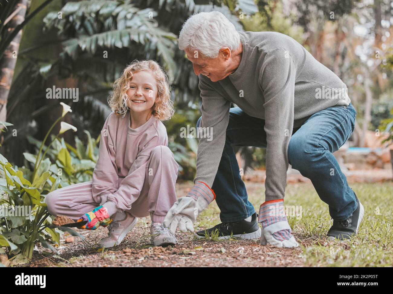 Großvater kennt die besten Gartengeheimnisse. Aufnahme eines entzückenden kleinen Mädchens, das mit ihrem Großvater im Garten arbeitet. Stockfoto