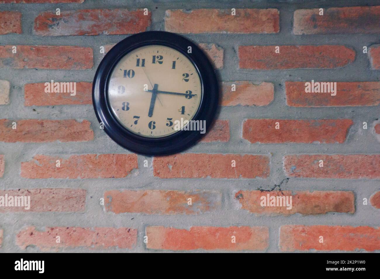 Die schwarze Uhr steht auf der alten Ziegelmauer. Stockfoto
