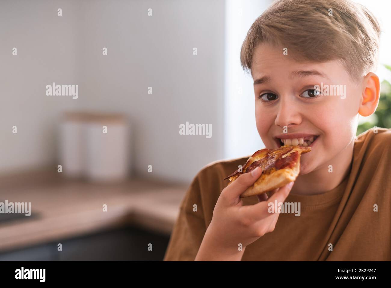 Fröhlicher Teenager, der zu Hause leckere Pizza genießt. Frisch gebackene Pepperoni Pizza Stockfoto