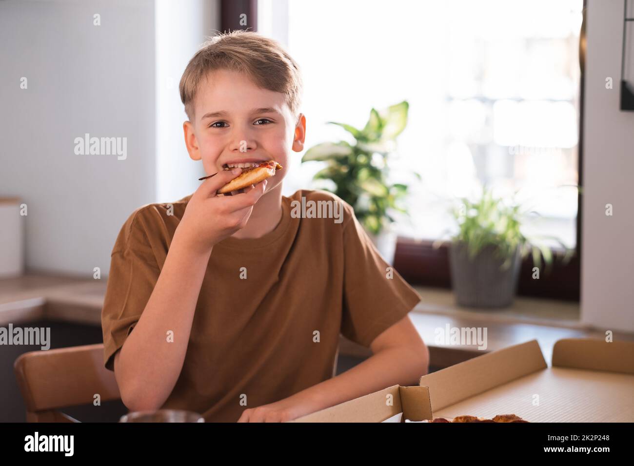 Fröhlicher Teenager, der zu Hause leckere Pizza genießt. Frisch gebackene Pepperoni Pizza Stockfoto