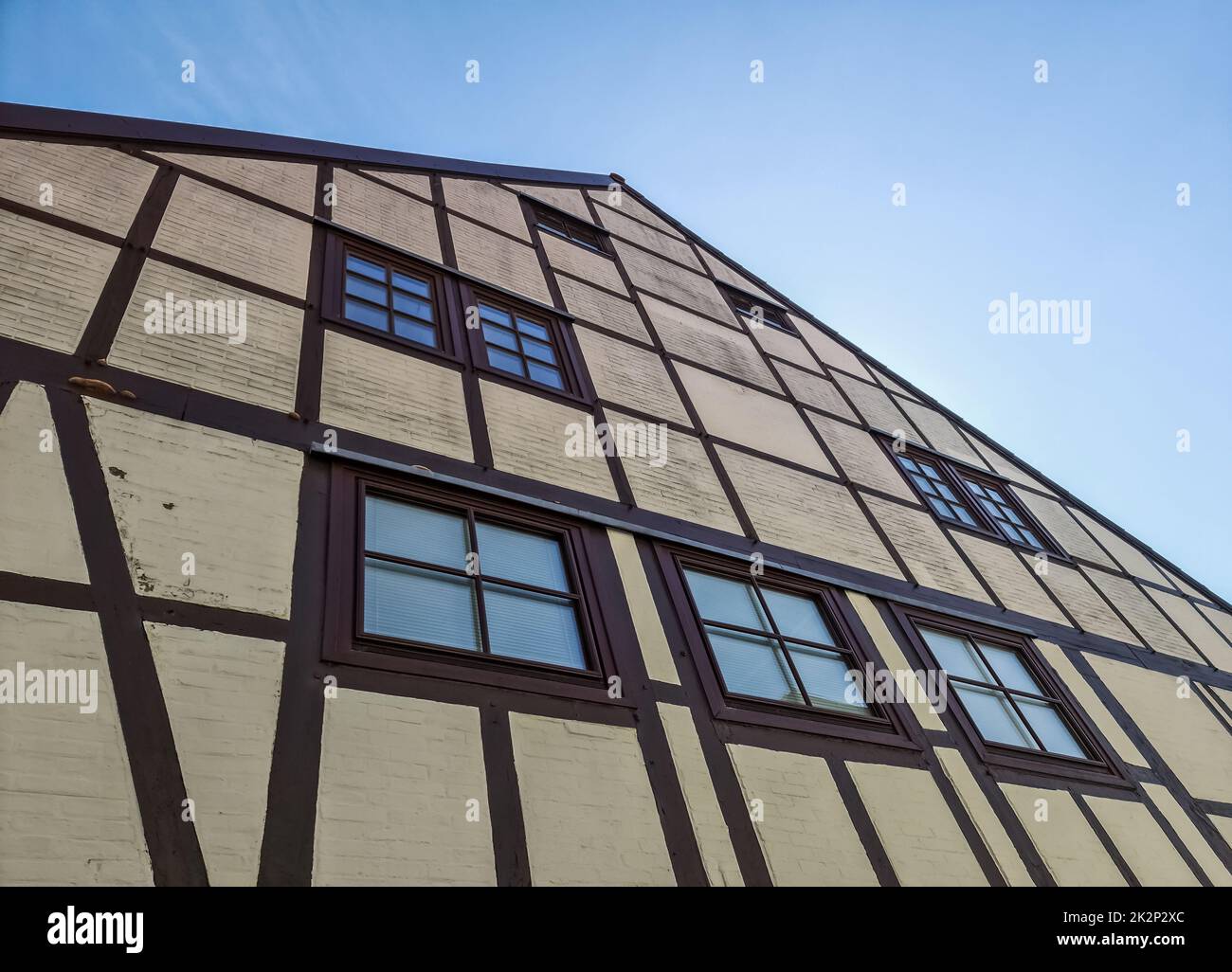 Blick aus einem niedrigen Winkel auf die Fassade des Hauses mit gelbem Stein und Halbholzbaumholz am blauen Himmel. Stockfoto