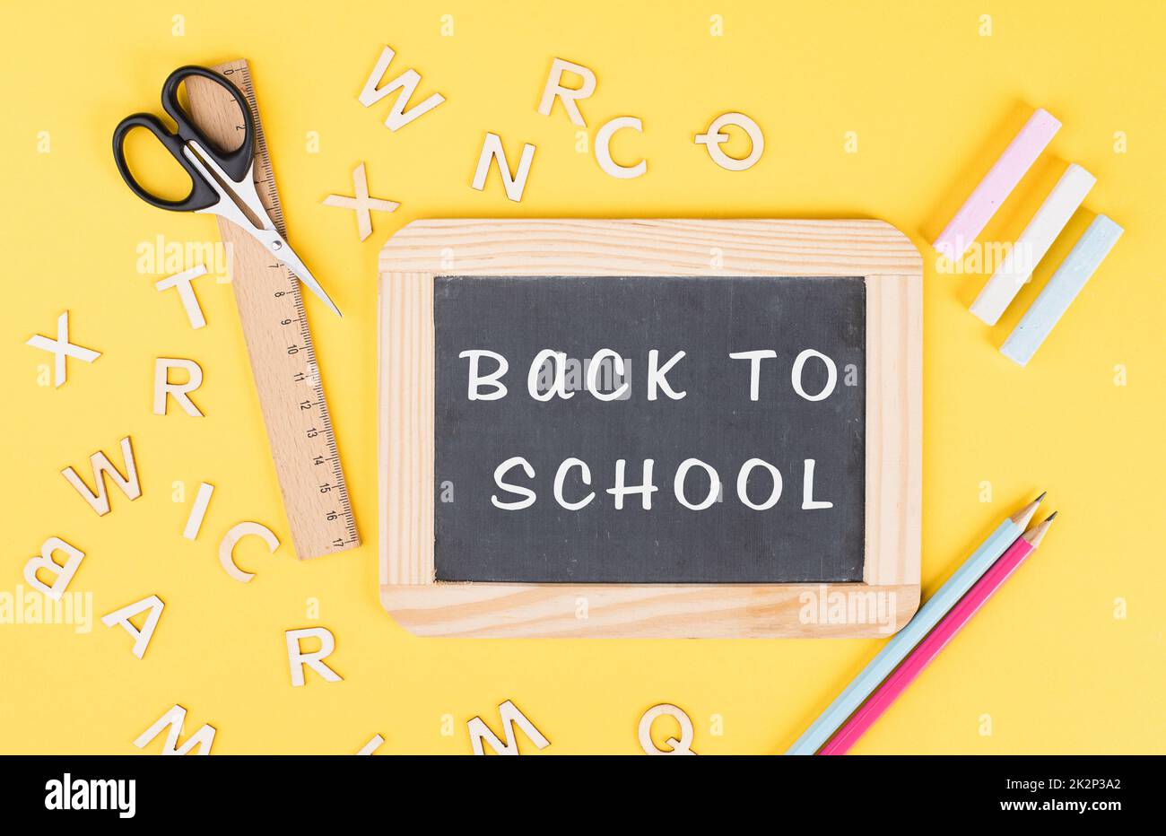 Leere Tafel mit bunter Kreide, Bleistiften, Lineal, Buchstaben und einer Schere, zurück zum Schul- und Bildungskonzept Stockfoto