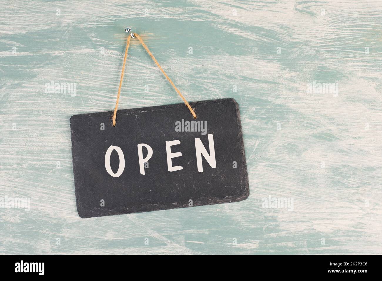 Das Wort Open steht auf einem Schild mit einer schwarzen Tafel, hängt an einer blau strukturierten verwitterten Tür, Konzept für Geschäfte, Geschäfte und Restaurants Stockfoto