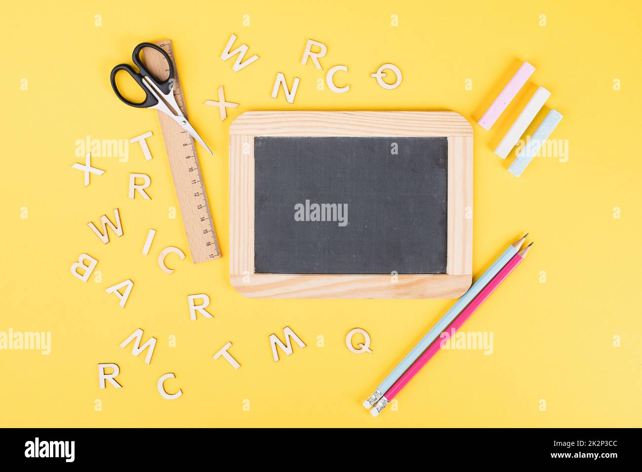 Leere Tafel mit bunter Kreide, Bleistiften, Lineal, Buchstaben und einer Schere, zurück zum Schul- und Bildungskonzept Stockfoto