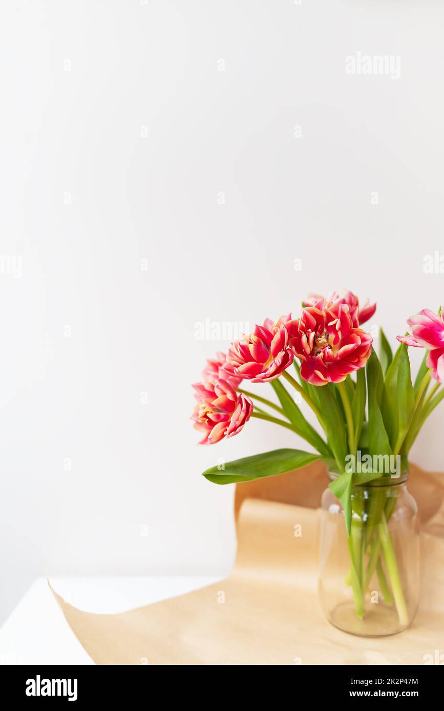 Ein wunderschöner Frühlingsstrauß aus Tulpen steht in einer Vase. Überraschungskonzept, Geburtstag. Vertikales Foto, Platz für eine Inschrift. Stockfoto