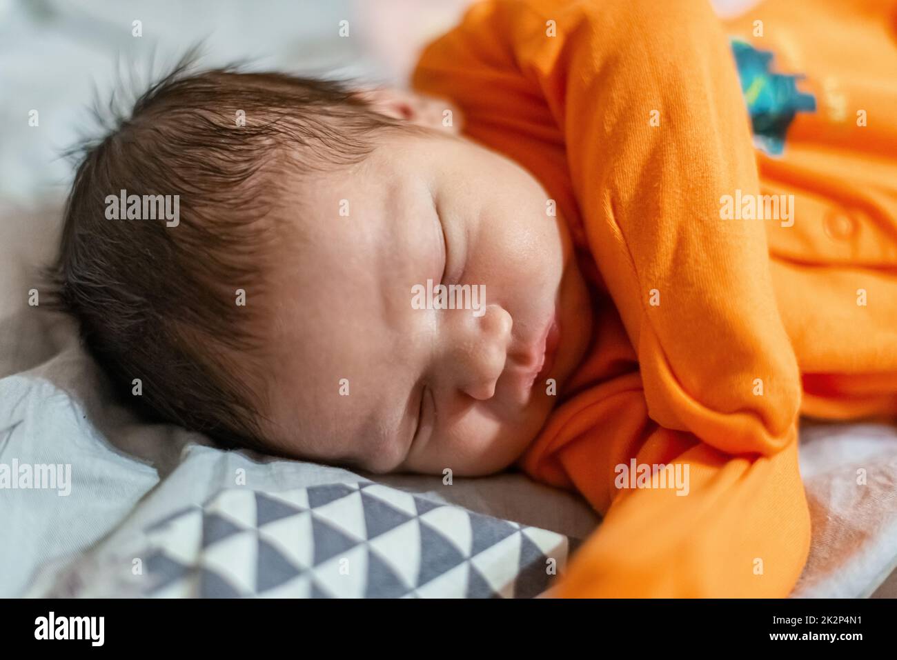 Das neugeborene Baby in Orange schliesst in seinem Bett Stockfoto