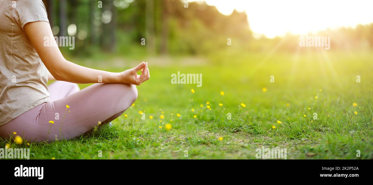 Frau, die in aktiver Kleidung in Lotusposition in der Natur sitzt. Stockfoto