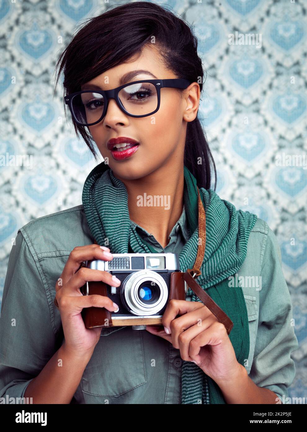 Eine junge Frau, die mit einer Kamera auf einem gemusterten Hintergrund posiert. Stockfoto