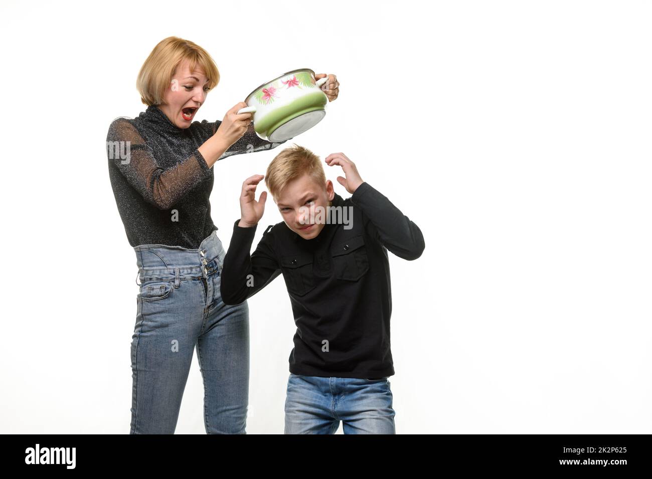 Mutter schlägt ihren Sohn mit einer Pfanne, weil er sich weigert, selbst gekochtes Essen zu essen Stockfoto