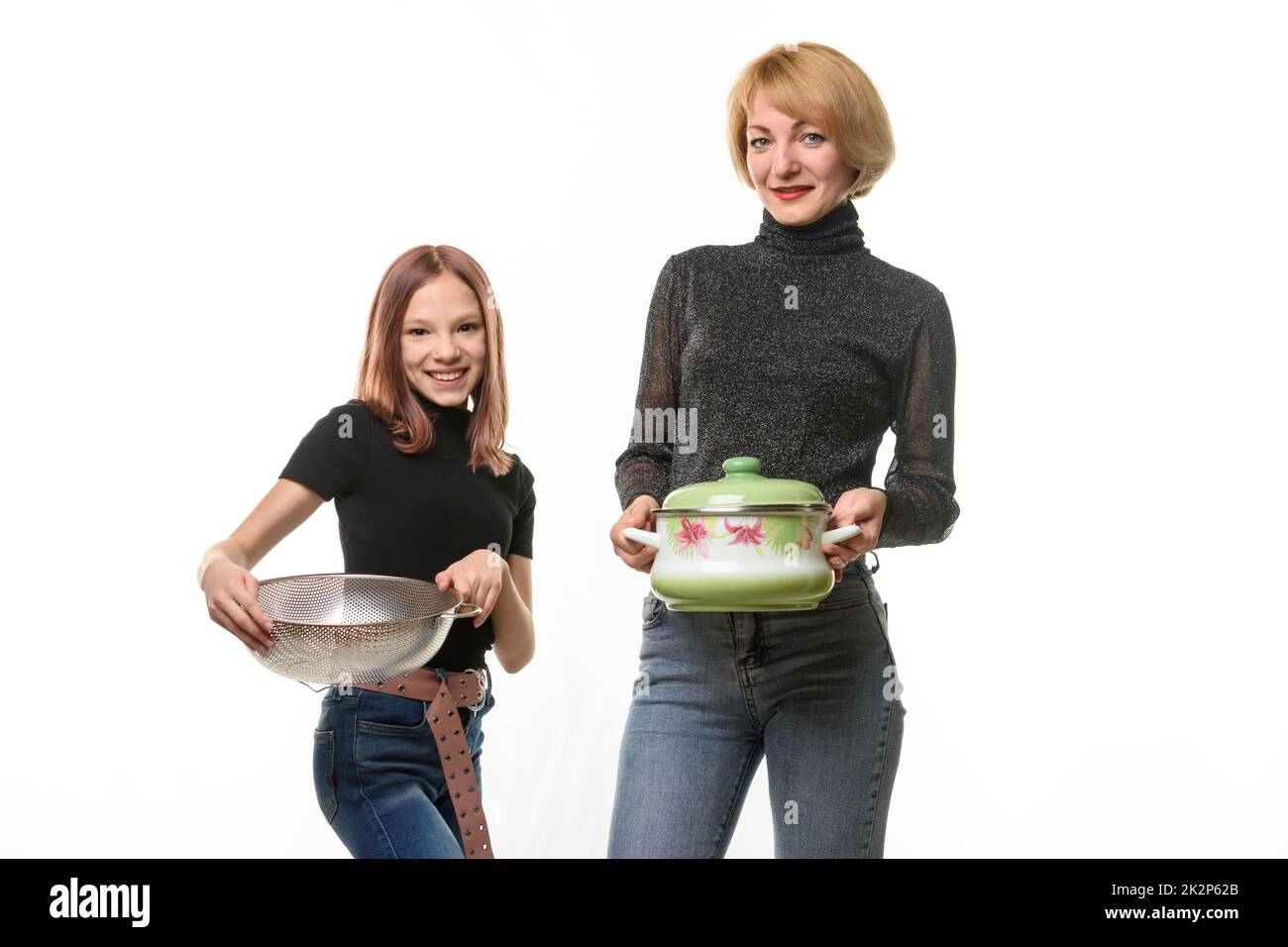 Mama steht mit einem Topf, Tochter steht mit einem Sieb, beide lächeln und blicken in den Rahmen Stockfoto