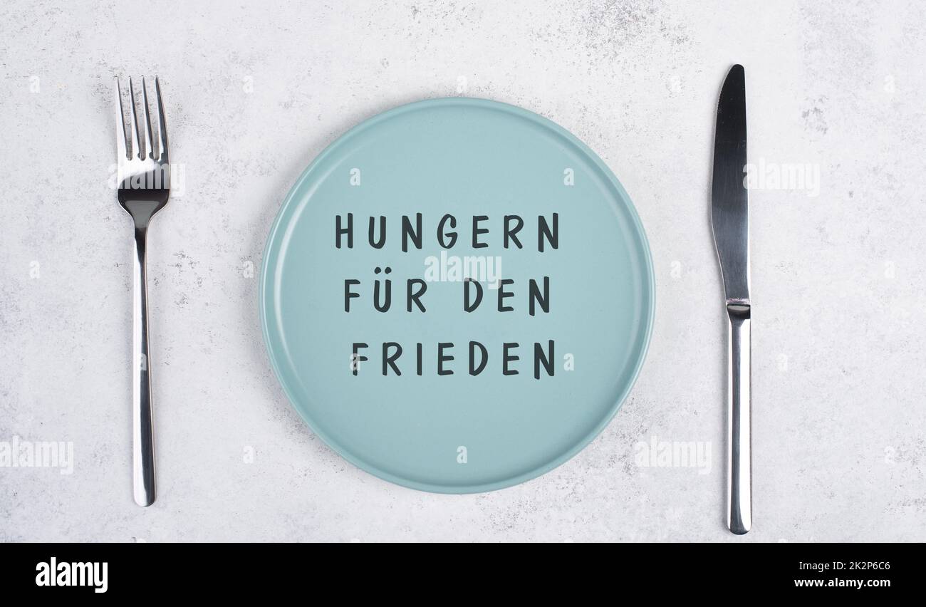 Hunger nach Frieden steht in deutscher Sprache auf dem leeren Teller, Lebensmittelknappheit durch den Krieg in der Ukraine, politische Frage Stockfoto