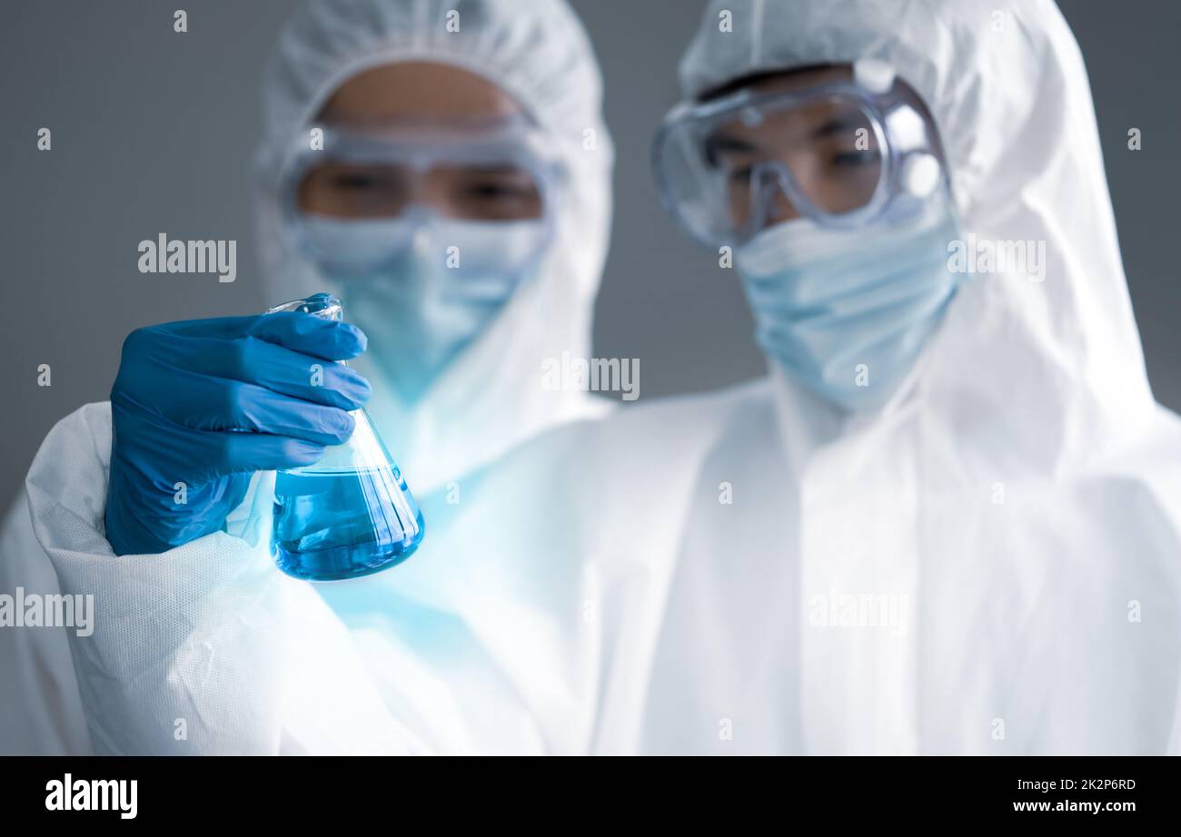 Covid-19-Testung im Labor. Zwei Wissenschaftler diskutieren über blaue flüssige Chemikalien in Erlenmeyerkolben. Blauer Lichteffekt. Gesundheitswesen und medizinisches Konzept. Stockfoto