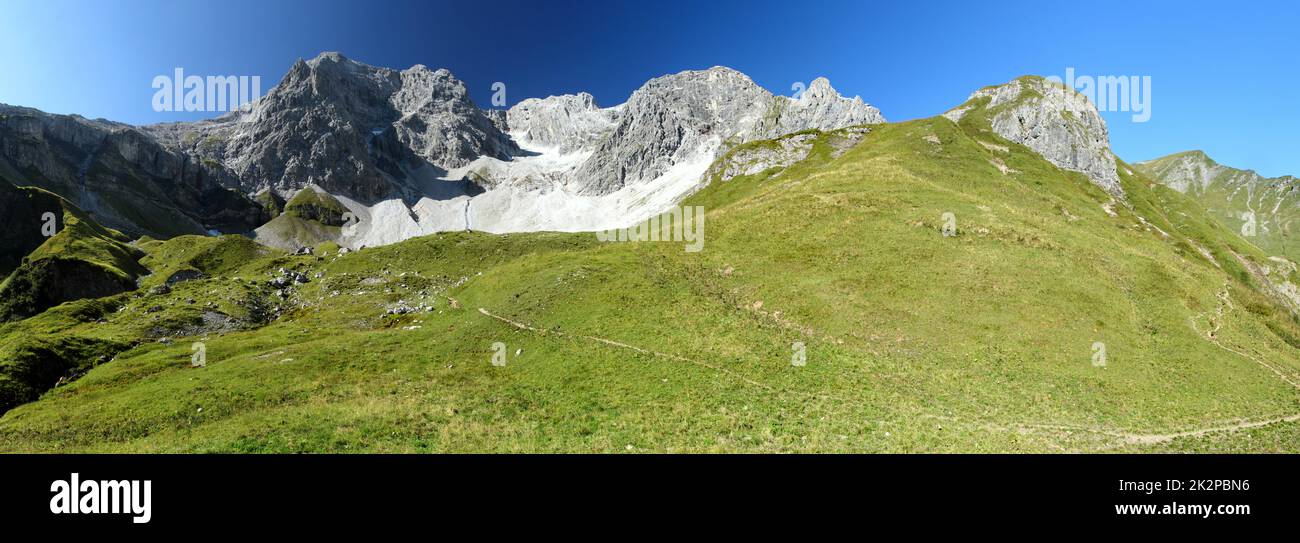 Panorama einer alpinen Landschaft mit blauem Himmel im Hintergrund und Gras im Vordergrund Stockfoto