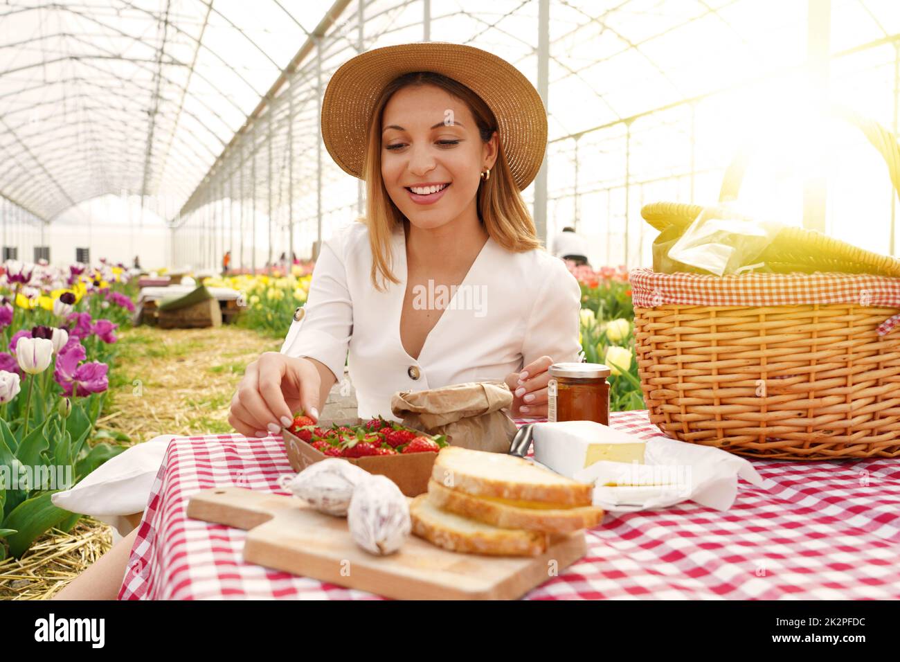 Lächelnd schönes Mädchen mit Picknick. Junge Frau nimmt eine Erdbeere. Frische Ernte und Null-Kilometer-Lebensmittel im Land im Frühling. Stockfoto