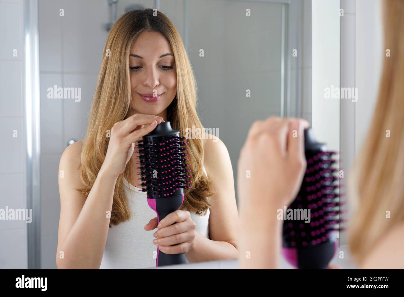 Zufrieden Mädchen hält Runde Bürste Haartrockner in ihrem Badezimmer zu Hause. Junge Frau hält ihren Salon ein-Schritt-Bürste Haartrockner und Volumenizer. Stockfoto