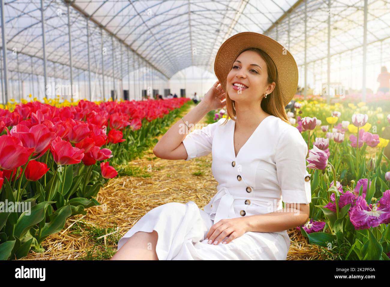 Ziemlich schönes Mädchen mit Strohhut sitzt zwischen Tulpen Feld im Gewächshaus Stockfoto
