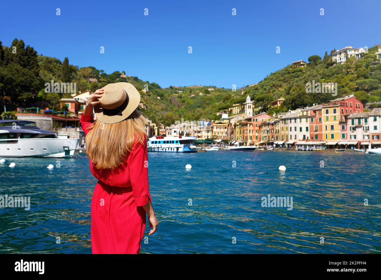 Tourismus in Italien. Rückansicht der wunderschönen jungen Frau in rotem Kleid bietet Blick auf das farbenfrohe Dorf Portofino mit Yachten im Hafen, Portofino, Ligurien, Italien. Stockfoto